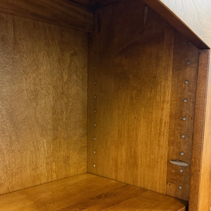 Close-up of the interior of a wooden bookshelf or cabinet, showing a warm medium-brown wood finish, a shelf divider, and visible screw holes along the side.