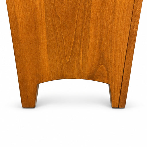 Close-up of the lower portion of a medium brown wooden furniture piece, showing the grain and curved front edge, standing on a gray carpeted floor.
