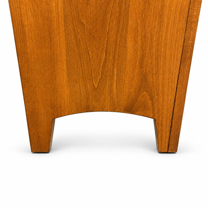 Close-up of the lower portion of a medium brown wooden furniture piece, showing the grain and curved front edge, standing on a gray carpeted floor.