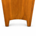 Close-up of the lower portion of a medium brown wooden furniture piece, showing the grain and curved front edge, standing on a gray carpeted floor.
