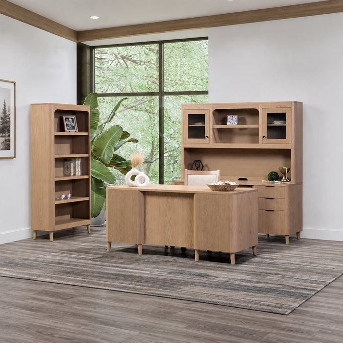 Wooden office furniture set with a desk, bookshelf, and cabinets in a bright room with large windows.