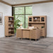 Wooden office furniture set with a desk, bookshelf, and cabinets in a bright room with large windows.