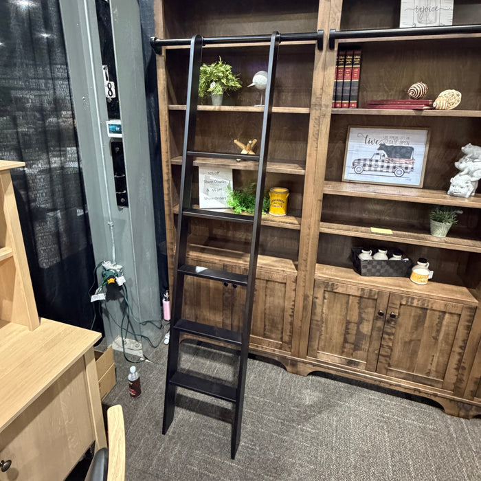 A rustic dark wood bookcase with a black metal ladder shelf, styled with books, plants, and decorative items in a showroom setting.