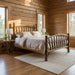 A rustic log-frame bed with a curved spindle headboard and footboard, dressed in a woodland camouflage patterned comforter and two matching pillows, photographed on a light gray studio background.