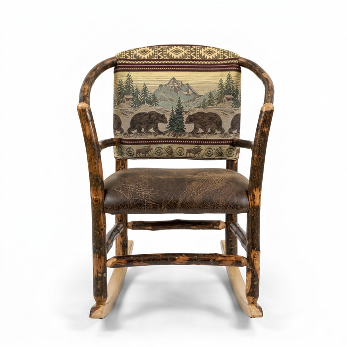 A rustic log-style rocking chair with a brown leather seat and a backrest featuring a green and beige bear and tree pattern, shown in a furniture store.