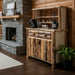 A rustic wooden hutch cabinet with a natural bark-edges finish, featuring a top shelf with six silver mugs, two upper drawers, and two lower cabinet doors with rustic metal handles, set against a light gray background.