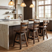 A rustic kitchen island with a light stone countertop and dark wood cabinetry, featuring three wooden bar stools with slatted backs. Three pendant lights hang above the island, and a large multi-pane window is visible in the background along with exposed wooden beams on the ceiling.