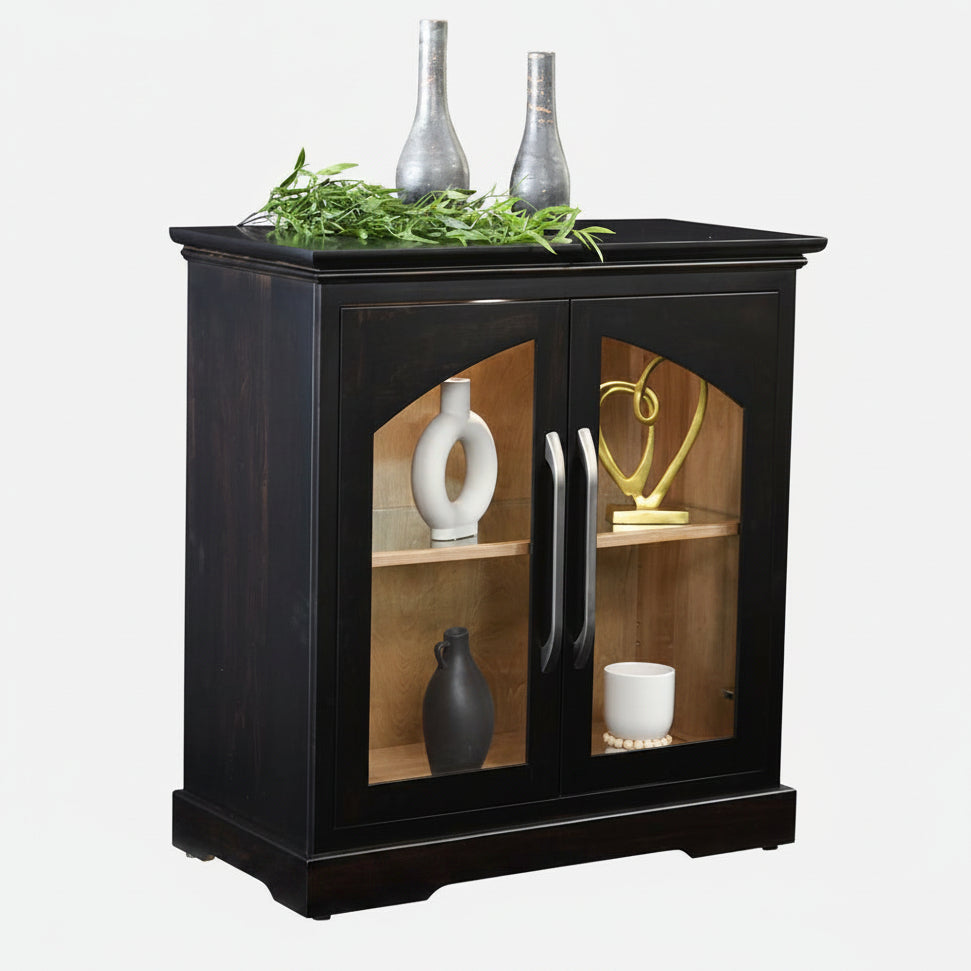 A black wooden side cabinet with two glass-front doors, styled with decorative vases and greenery on top, shown against a plain white background.