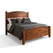 A wooden bed frame with a curved headboard and footboard, styled with a dark gray comforter, white sheets, and decorative pillows in a bright, modern bedroom.