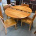 A light natural wood oval dining table with four matching curved-back wooden chairs, photographed in a furniture showroom.