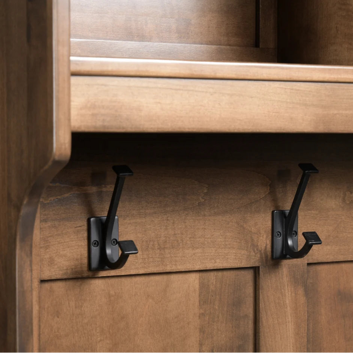 Three matte black metal coat hooks mounted on a warm brown wooden cabinet door under a shelf.