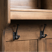 Three matte black metal coat hooks mounted on a warm brown wooden cabinet door under a shelf.