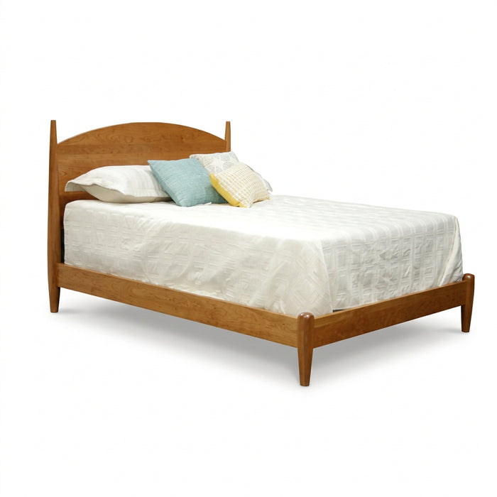 A mid-century modern wooden bed frame with a curved headboard and tapered legs, styled with white bedding and decorative pillows on a solid white background.