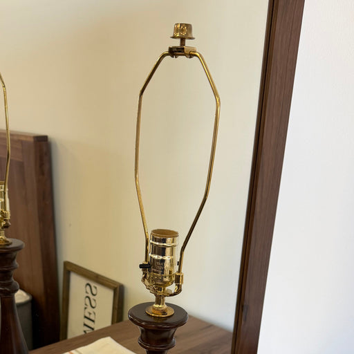 Wooden floor lamp with gold base and shade on a striped rug.