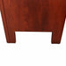 Close-up of the lower corner of a reddish-brown wooden furniture piece, likely a desk or cabinet, standing on a gray carpeted floor.
